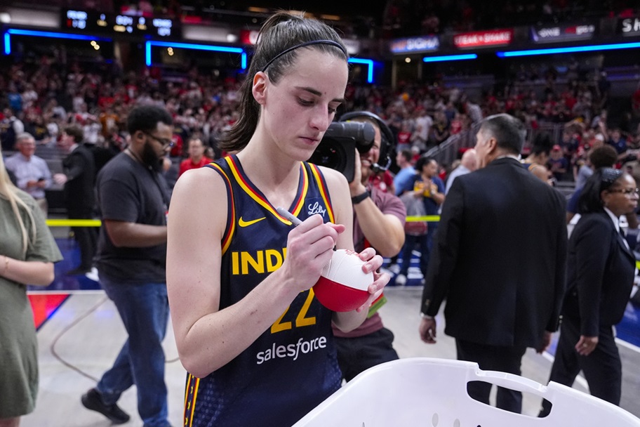 Caitlin Clark signs mini-basketballs for fans.